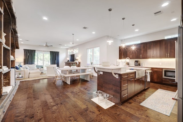 kitchen featuring dark hardwood / wood-style flooring, pendant lighting, a kitchen island with sink, ceiling fan, and dark brown cabinets