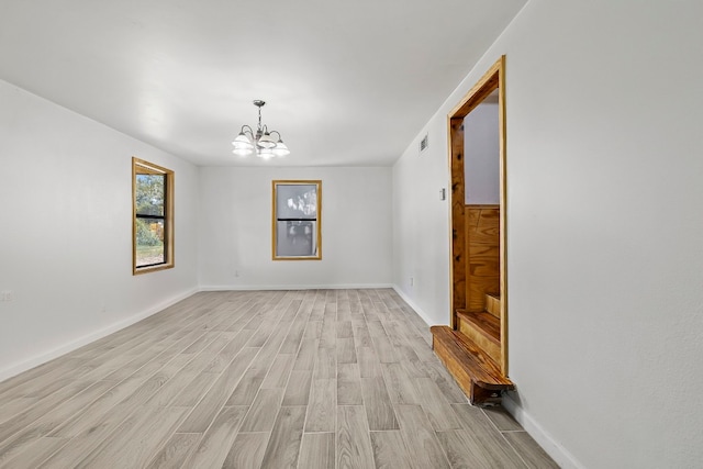 spare room featuring light wood-type flooring and a chandelier