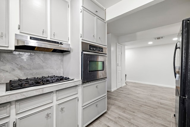 kitchen featuring appliances with stainless steel finishes, white cabinetry, light hardwood / wood-style flooring, and decorative backsplash