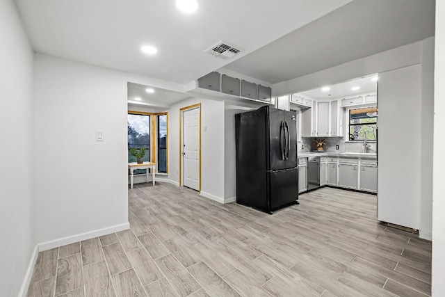 kitchen featuring black refrigerator, dishwasher, light wood-type flooring, and decorative backsplash