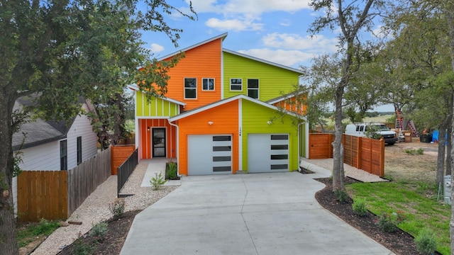 contemporary home featuring board and batten siding, fence, driveway, and an attached garage