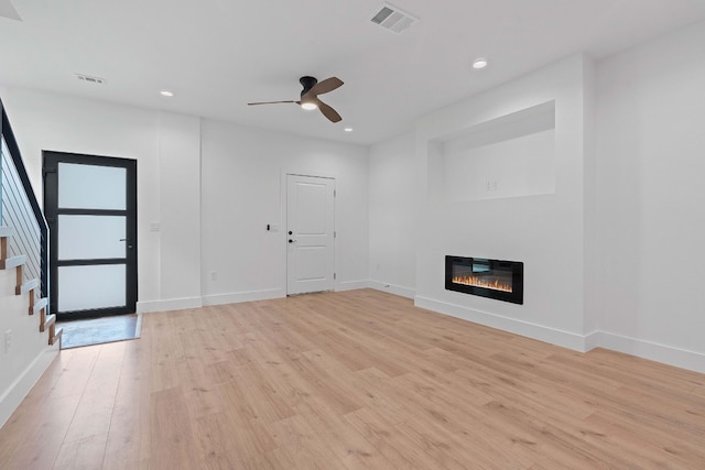 unfurnished living room featuring light wood-style flooring, visible vents, baseboards, and a glass covered fireplace