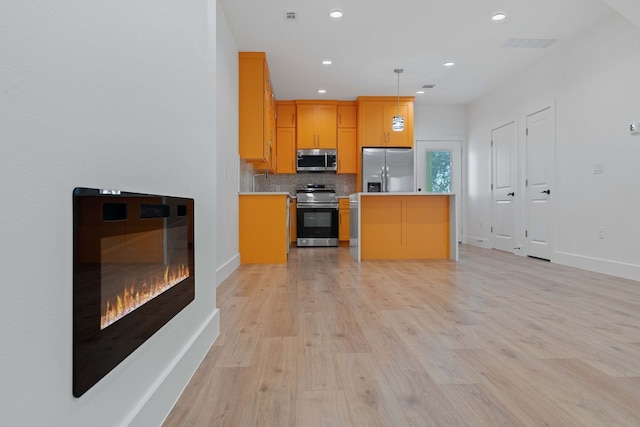 kitchen with pendant lighting, tasteful backsplash, light countertops, appliances with stainless steel finishes, and light wood-style floors