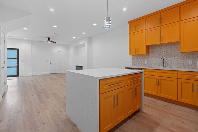 kitchen with sink, light hardwood / wood-style flooring, ceiling fan, a kitchen island, and decorative light fixtures