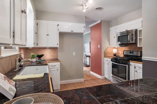 1511 Fairfield Dr, Austin, TX 78757 - kitchen featuring appliances with stainless steel finishes, a sink, white cabinets, light tile patterned floors, and tasteful backsplash