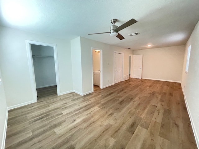 unfurnished bedroom featuring ensuite bath, a textured ceiling, ceiling fan, light wood-type flooring, and a walk in closet