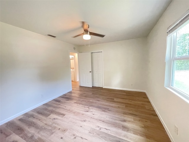 unfurnished bedroom featuring multiple windows, light hardwood / wood-style floors, ceiling fan, and a closet