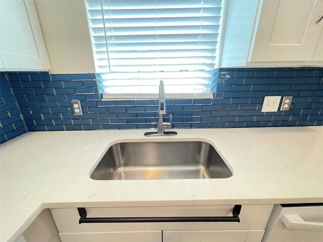 details featuring tasteful backsplash, white cabinetry, and sink