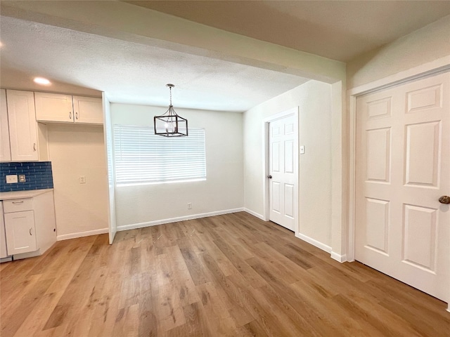 unfurnished dining area featuring a chandelier, a textured ceiling, and light hardwood / wood-style floors