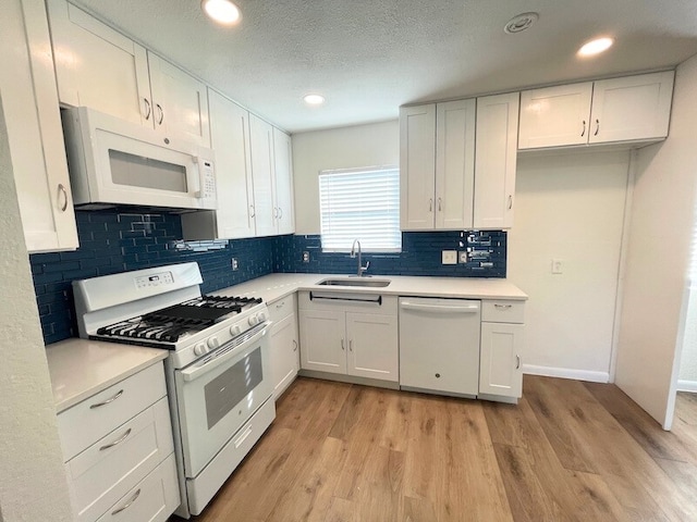 kitchen with sink, white appliances, white cabinets, light wood-type flooring, and decorative backsplash