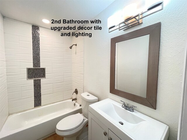 full bathroom featuring tiled shower / bath, a textured ceiling, toilet, and vanity