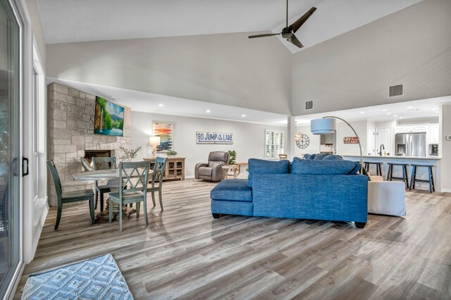 living room with high vaulted ceiling, ceiling fan, a fireplace, and light hardwood / wood-style floors