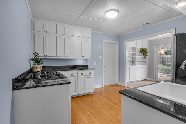 kitchen featuring light hardwood / wood-style flooring, white cabinets, crown molding, stainless steel fridge, and black gas cooktop