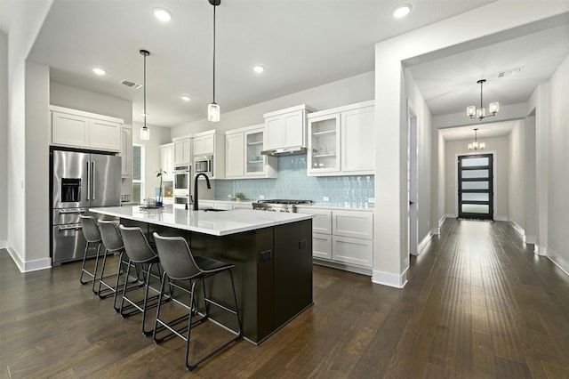 kitchen featuring dark wood-type flooring, white cabinets, stainless steel appliances, and a center island with sink