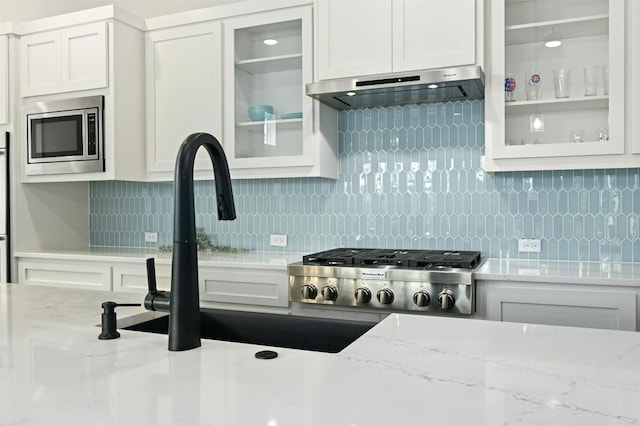 kitchen featuring stainless steel appliances, light stone counters, decorative backsplash, and white cabinets