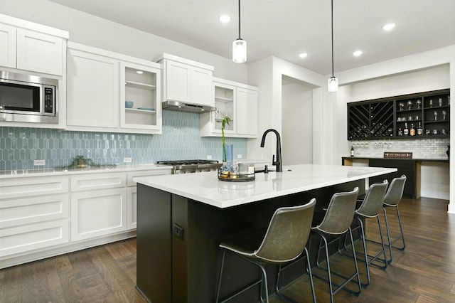 kitchen with stainless steel appliances, decorative light fixtures, dark wood-type flooring, a center island with sink, and white cabinets