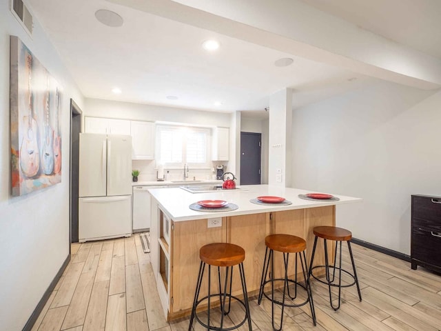 kitchen with light hardwood / wood-style flooring, a center island, white refrigerator, a breakfast bar area, and white cabinets