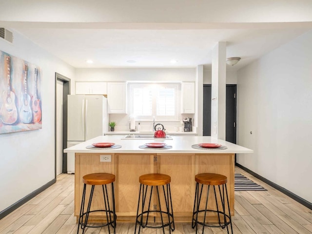 kitchen featuring light hardwood / wood-style floors, white cabinetry, a center island, and a breakfast bar