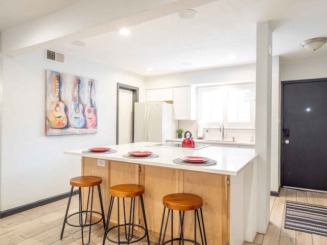 kitchen featuring a kitchen bar, a kitchen island, white fridge, and light wood-type flooring