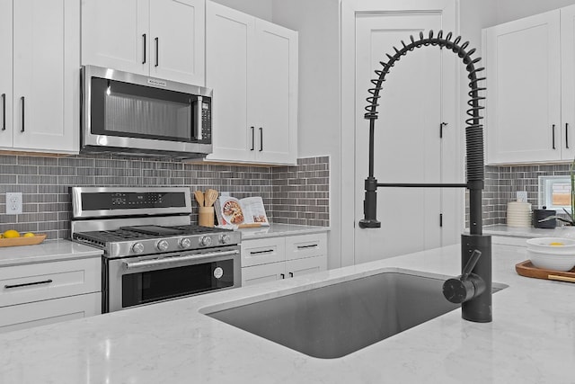 kitchen with stainless steel appliances, light stone counters, backsplash, and white cabinets