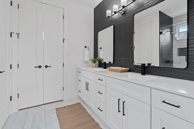 full bath featuring double vanity, marble finish floor, a sink, and tiled shower