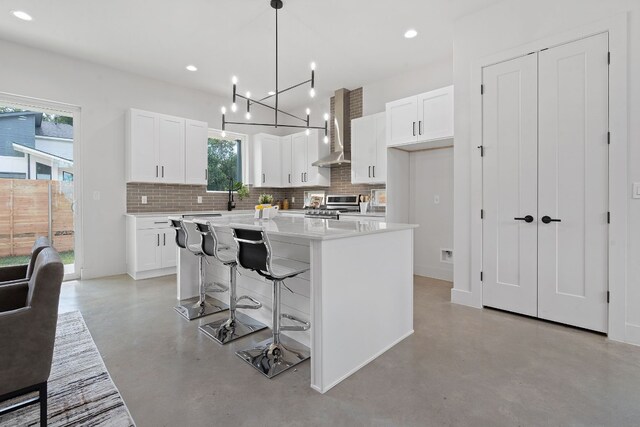 kitchen featuring plenty of natural light, a kitchen island, wall chimney range hood, and white cabinetry