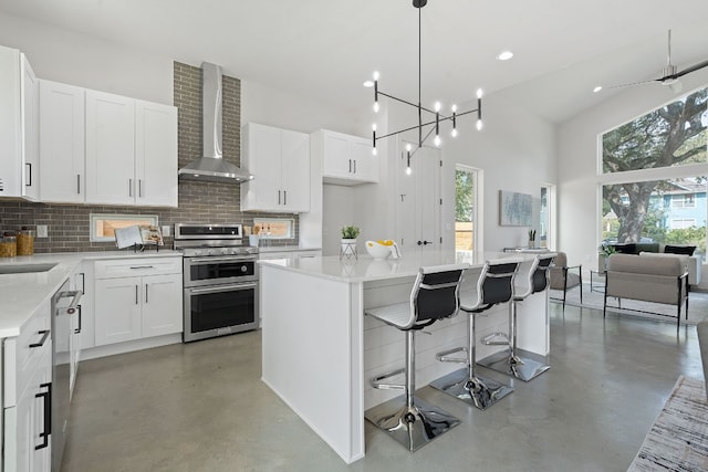 kitchen with a center island, stainless steel appliances, wall chimney exhaust hood, and white cabinetry