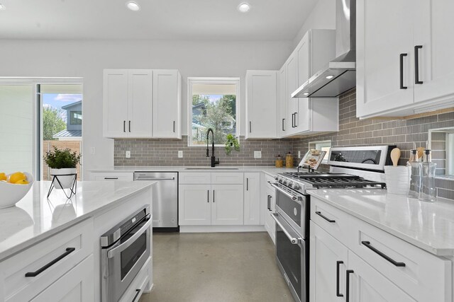 kitchen featuring stainless steel appliances, wall chimney exhaust hood, white cabinetry, and sink