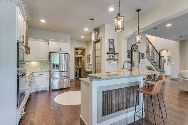 kitchen with white cabinets, appliances with stainless steel finishes, light stone counters, dark hardwood / wood-style floors, and a breakfast bar