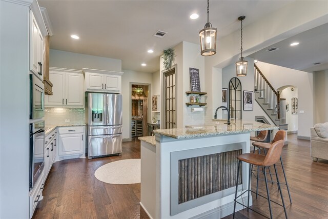 kitchen featuring light stone counters, white cabinetry, hanging light fixtures, appliances with stainless steel finishes, and an island with sink