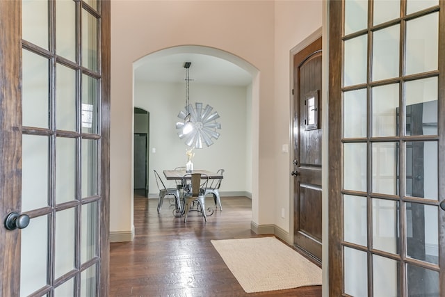 entryway featuring arched walkways, a chandelier, dark wood-style floors, and baseboards