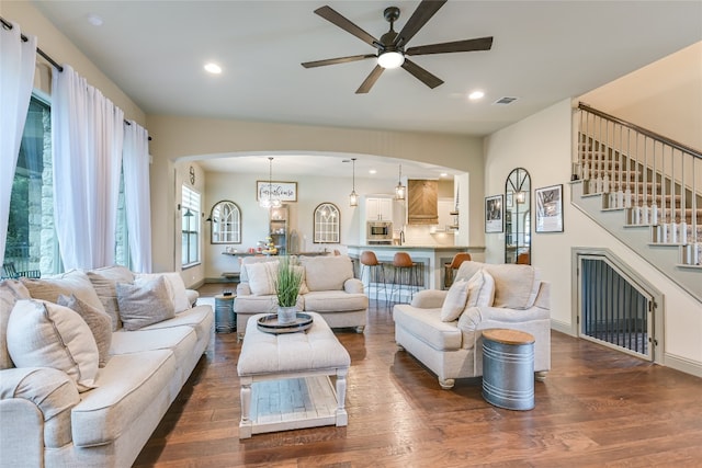 living room featuring ceiling fan with notable chandelier and dark wood-type flooring