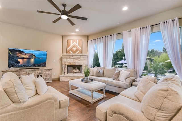 living room with wood-type flooring, ceiling fan, and a stone fireplace