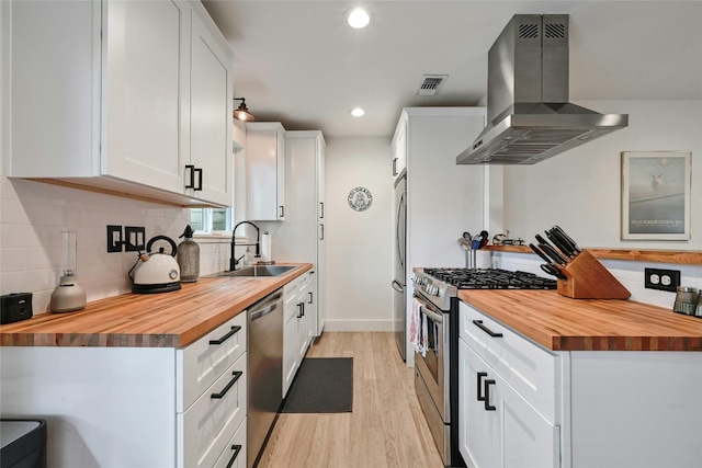 kitchen with white cabinetry, sink, wooden counters, exhaust hood, and appliances with stainless steel finishes