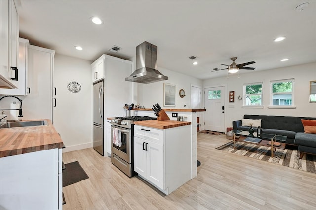 kitchen featuring butcher block counters, sink, wall chimney exhaust hood, white cabinetry, and stainless steel appliances