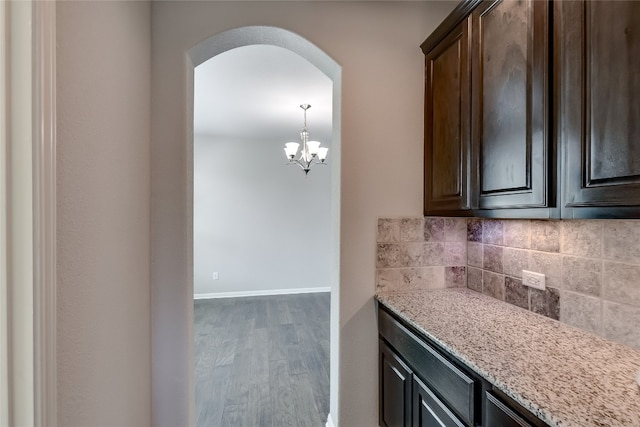 kitchen with backsplash, light stone countertops, dark brown cabinets, and dark hardwood / wood-style floors