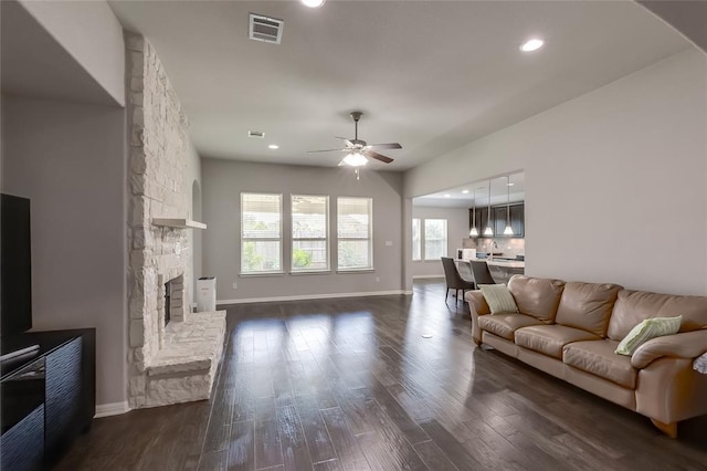 living room with dark hardwood / wood-style floors, a stone fireplace, and ceiling fan