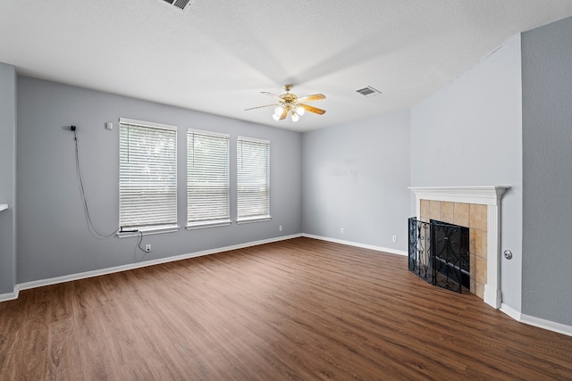 unfurnished living room featuring a tile fireplace, a textured ceiling, dark hardwood / wood-style flooring, and ceiling fan