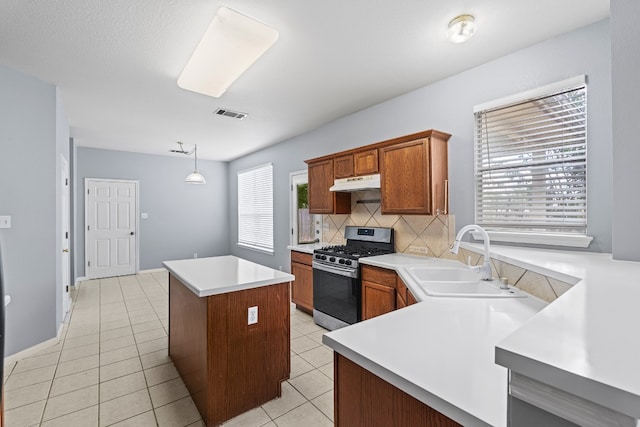 kitchen featuring backsplash, sink, light tile patterned floors, decorative light fixtures, and stainless steel range with gas stovetop