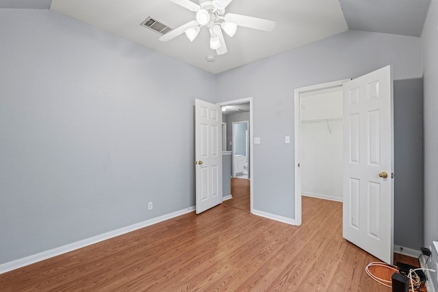 unfurnished bedroom with ceiling fan, a spacious closet, vaulted ceiling, a closet, and light wood-type flooring