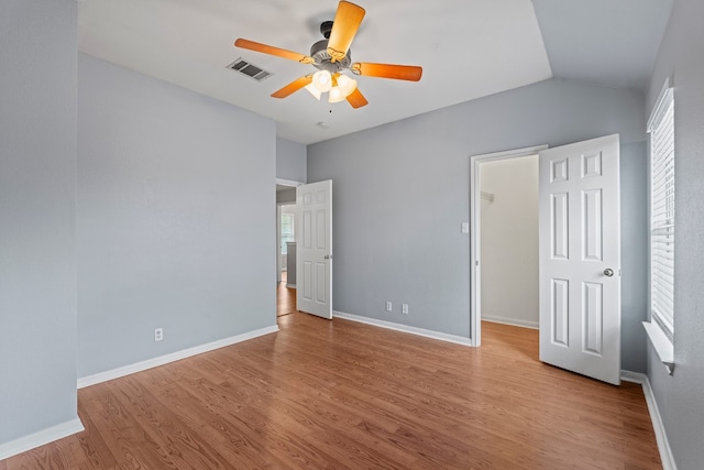 unfurnished bedroom featuring ceiling fan, light wood-type flooring, a walk in closet, and multiple windows