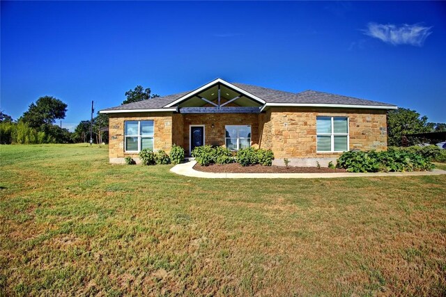 ranch-style house with a shingled roof, stone siding, and a front lawn