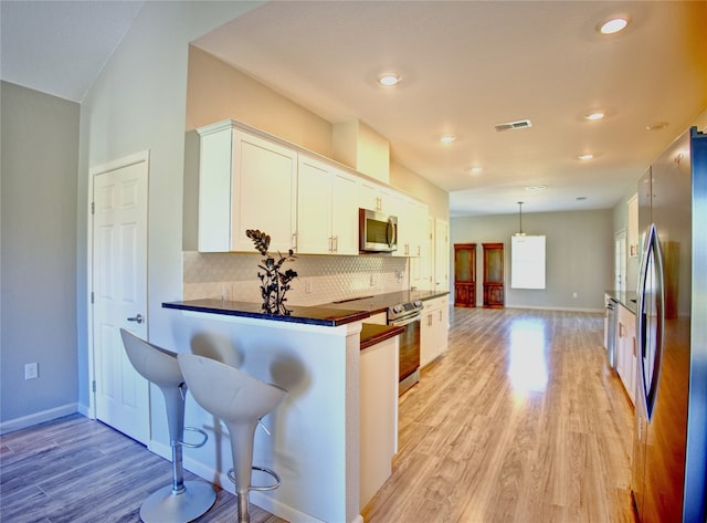 kitchen with light wood-type flooring, kitchen peninsula, appliances with stainless steel finishes, a breakfast bar area, and white cabinets