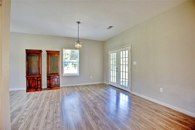 unfurnished dining area featuring light hardwood / wood-style floors, a notable chandelier, and french doors