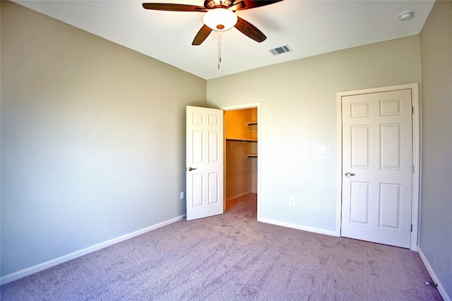 unfurnished bedroom featuring a walk in closet, a closet, ceiling fan, and light colored carpet