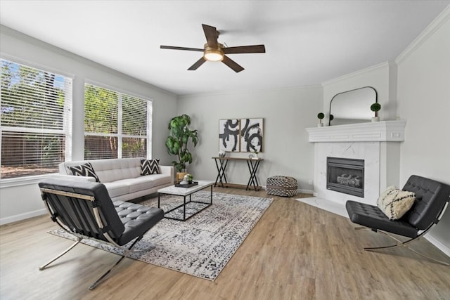 living room with ceiling fan, light hardwood / wood-style flooring, ornamental molding, and a high end fireplace