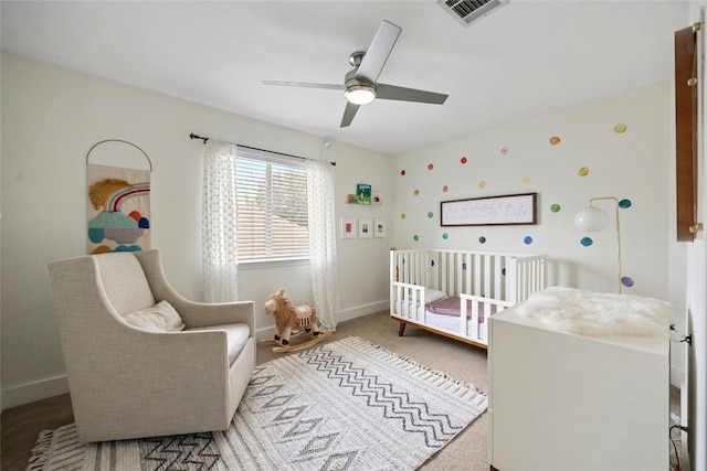 bedroom featuring ceiling fan, a nursery area, and light carpet