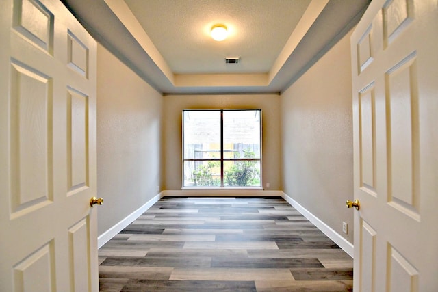 unfurnished room featuring a textured ceiling, hardwood / wood-style floors, and a tray ceiling