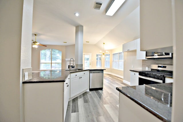 kitchen with ceiling fan with notable chandelier, stainless steel appliances, sink, dark stone counters, and kitchen peninsula