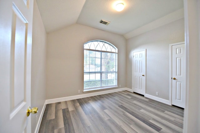 empty room featuring lofted ceiling, hardwood / wood-style flooring, and a textured ceiling